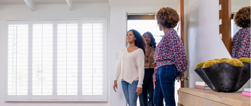 A relator holds the door of a new home open as two potential buyers walk in to the front room