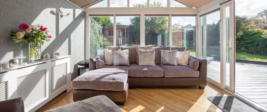 A comfortable couch is displayed inside an open and bright sunroom.