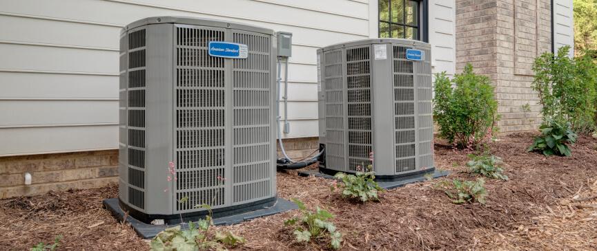 Two American Standard outdoor HVAC units sit on a bed of mulch and woodchips