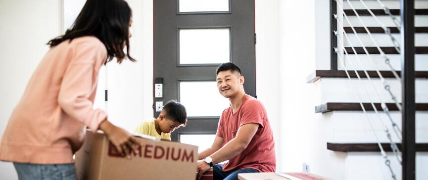 A woman holds a moving box as a man and child continue to pack more boxes