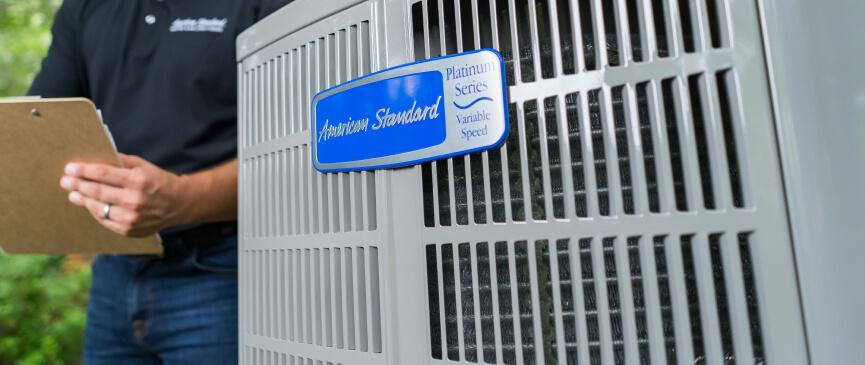 A Platinum Variable Speed American Standard air conditioner is pictured with an HVAC technician in the background