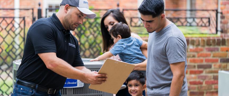 An HVAC technician shows a family information about their new American Standard HVAC system on his clipboard