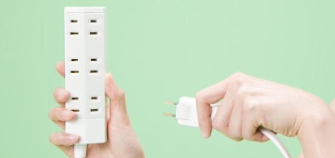 Hands holding an electrical power strip against a green background.