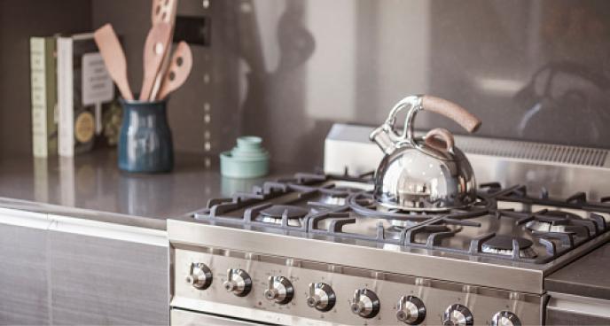 A stainless steel gas stove with a tea kettle sitting on top.