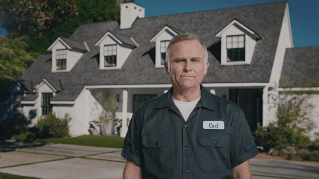 A middle-aged caucasian male hvac technician is standing in front of a white 2-story house.