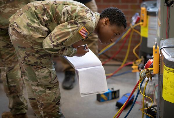 A young, female African American in an Army uniform is performing HVAC maintenance on a furnace.