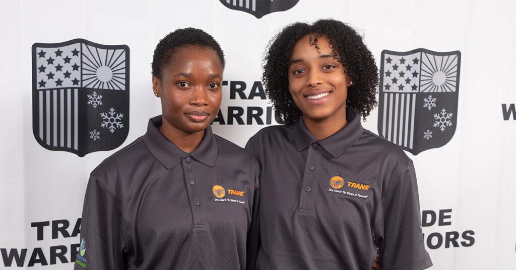 Two young African American women in black shirts are standing and smiling.