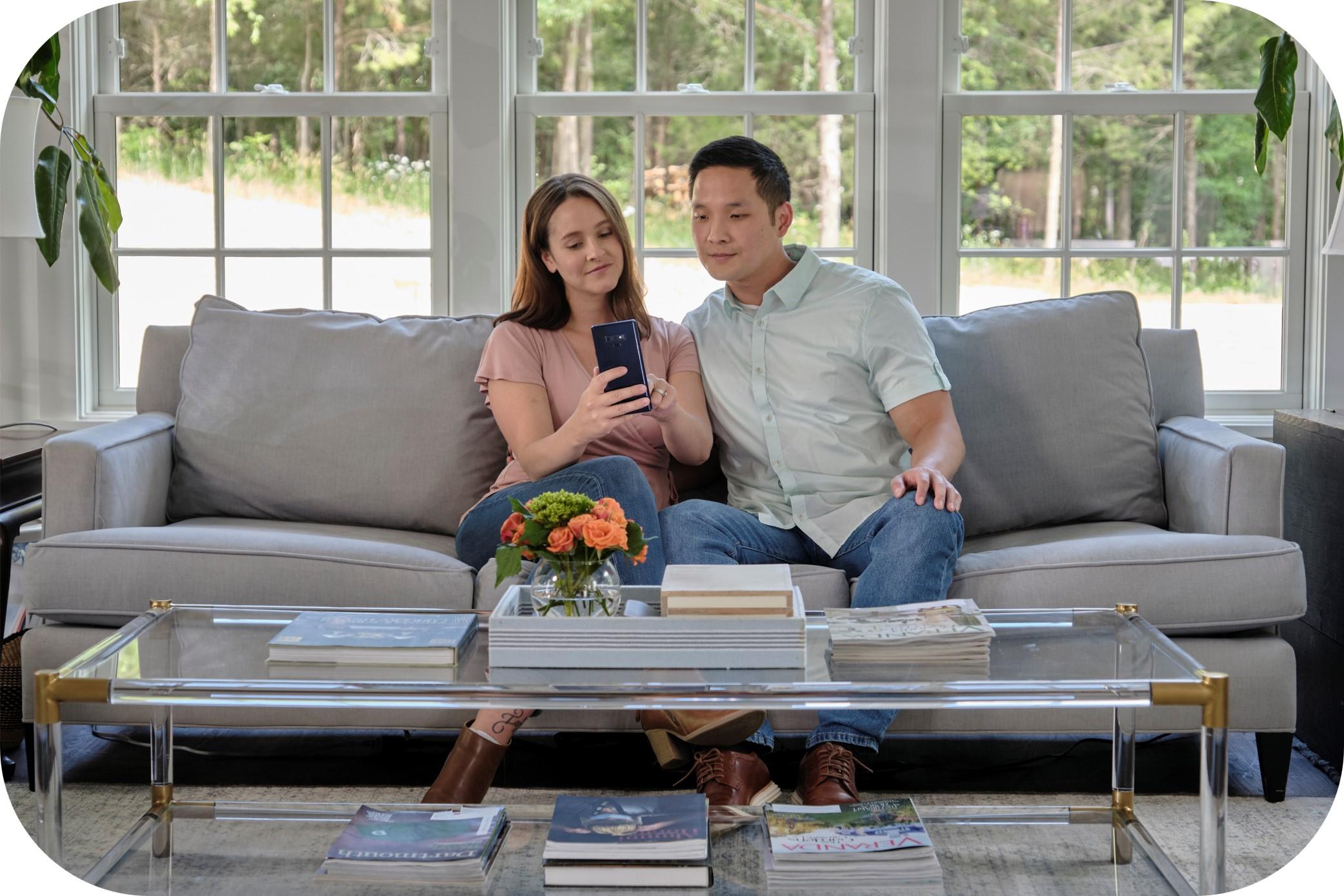 A young couple is seated on their gray couch.